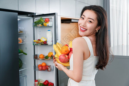 拿着水果的青年女人站在冰箱前美女高清图片素材