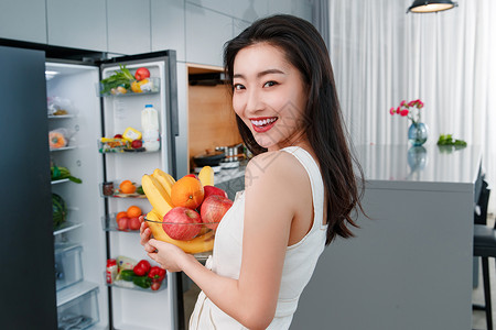 拿着水果的青年女人站在冰箱前家高清图片素材
