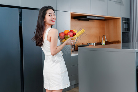拿着水果的青年女人站在冰箱前健康食物高清图片素材