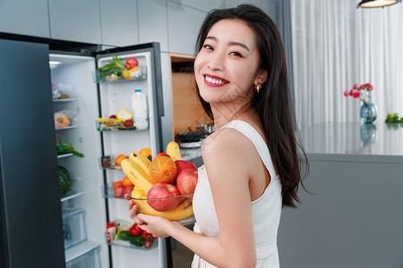 拿着水果的青年女人站在冰箱前减肥高清图片素材