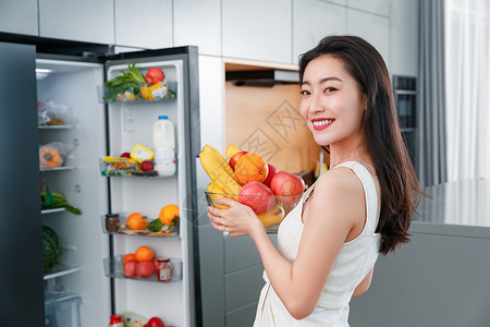拿着水果的青年女人站在冰箱前健康生活方式高清图片素材