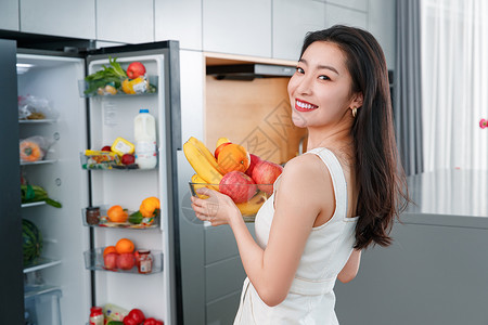 拿着水果的青年女人站在冰箱前中国高清图片素材