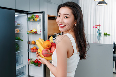 拿着水果的青年女人站在冰箱前快乐高清图片素材