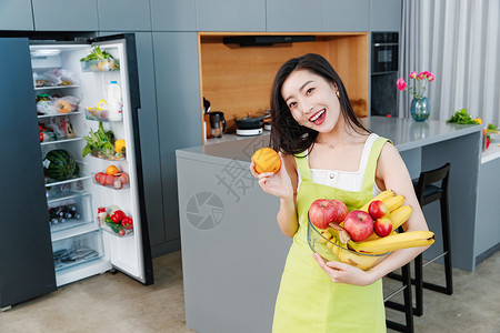 拿着水果的青年女人站在冰箱前食品高清图片素材