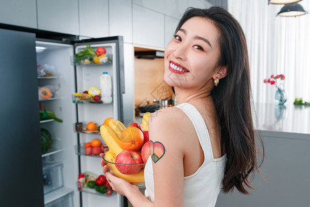 拿着水果的青年女人站在冰箱前橙子高清图片素材