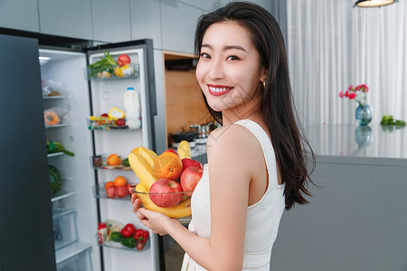 拿着水果的青年女人站在冰箱前东方人高清图片素材
