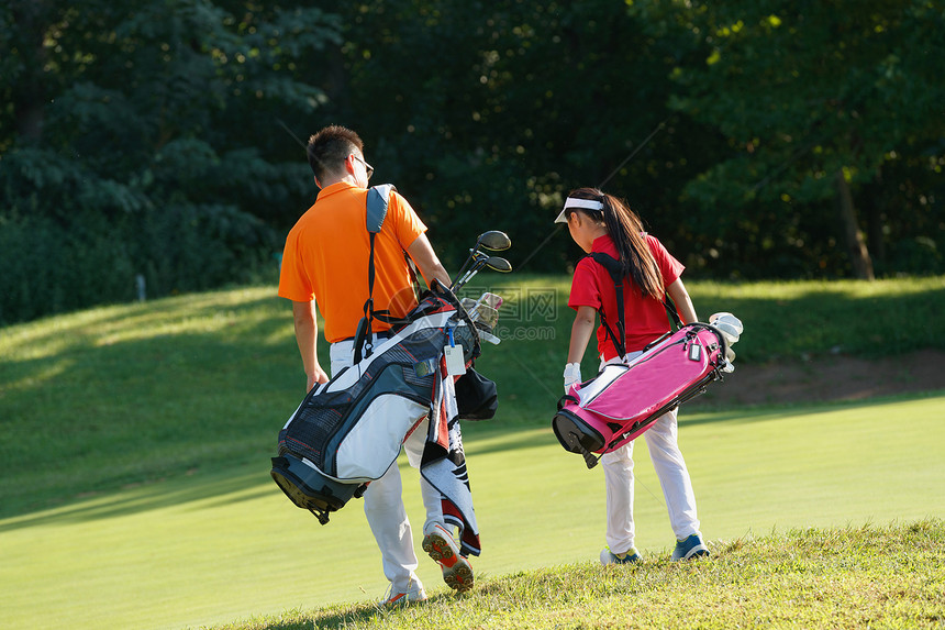 球场上教练和学生背着高尔夫球包步行的背影图片