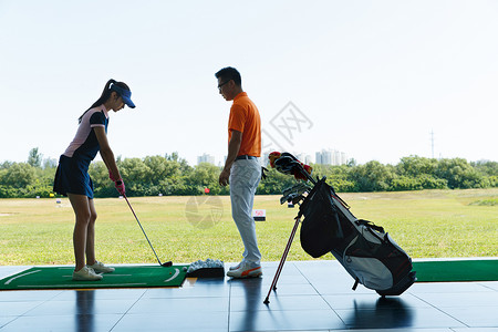 男人女人打球练习场上教练指导青年女人打高尔夫背景