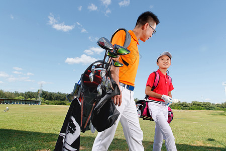 背着包的男孩球场上教练和学生背着高尔夫球包行走背景