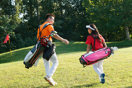 球场上教练和学生背着高尔夫球包行走高清图片
