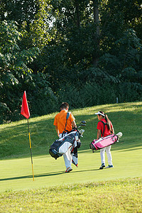 水上步行球球场上教练和学生背着高尔夫球包步行的背影背景
