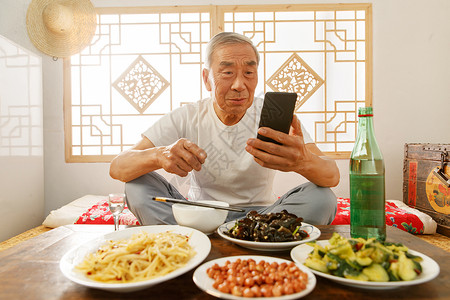 老年人坐在家里吃饭看手机图片素材