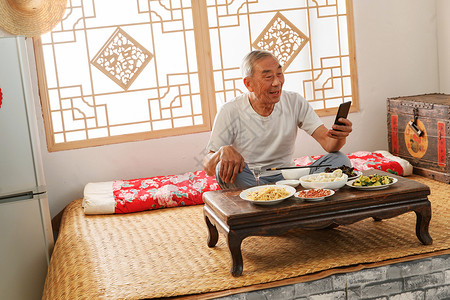 老年人坐在家里吃饭看手机图片素材