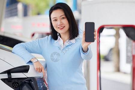 女性靠在新能源汽车旁展示手机屏幕高清图片