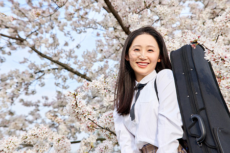 樱花树下背着乐器包的女性高中生高清图片