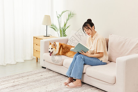 狗狗和爱心枕头客厅里看书的青年女性和宠物柯基背景