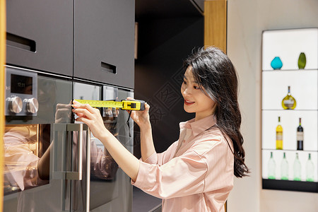 测量厨房冰箱的女性图片