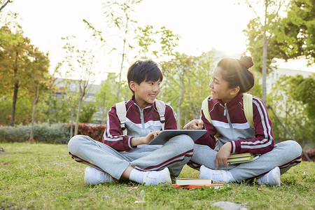 坐草地上的小学生使用平板电脑学习高清图片