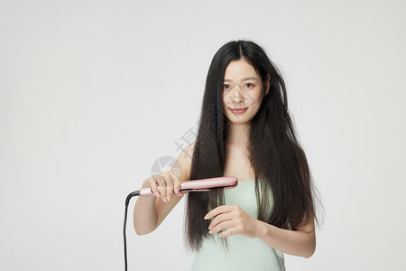 直板年轻女性使用夹板拉直头发背景
