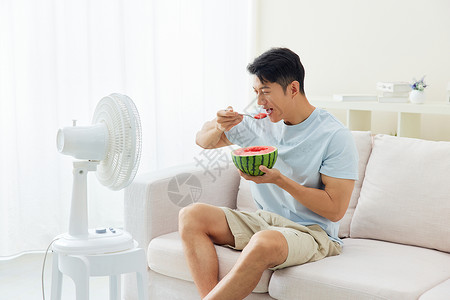 靠在沙发上吃西瓜吹风扇的男人避暑高清图片素材