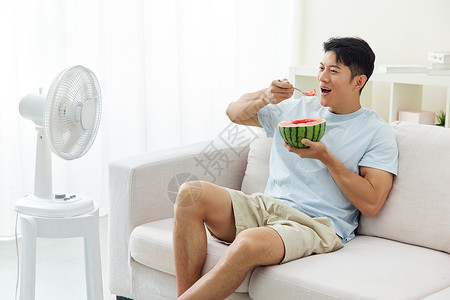 居家吃西瓜吹风扇的男人炎热高清图片素材