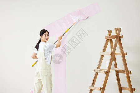 粉色墙面女子使用工具刷墙壁形象背景