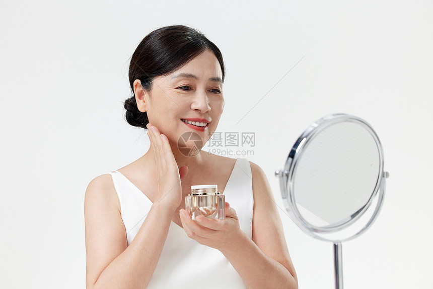 照镜子涂抹乳液的中年女性图片