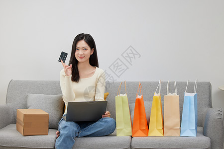 年中购物狂欢沙发上拿着购物卡与电脑的女性背景