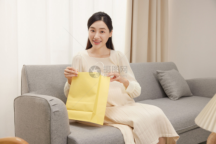 沙发上拿着购物袋的孕妇图片