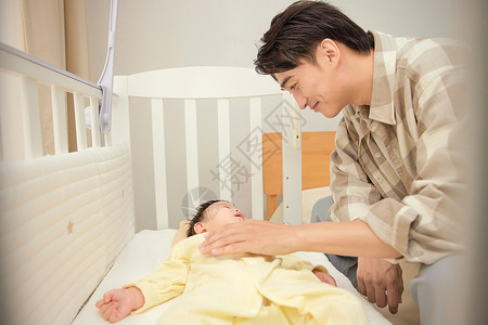 爸爸哄婴儿床里的宝宝睡觉背景图片