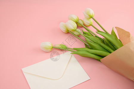 温馨花边素材粉色桌面上的白色信封和郁金香背景