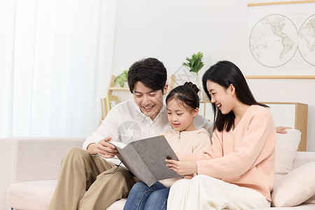 父母读书陪女儿认真看故事书的年轻父母背景