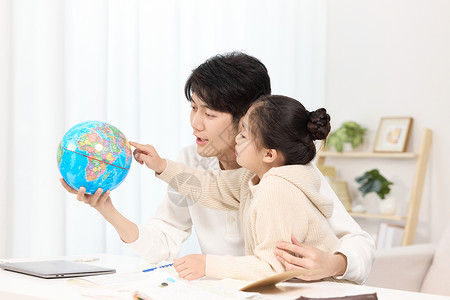 电脑室内正拿着地球仪给女儿讲解的年轻爸爸背景