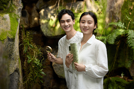 学习研究一对情侣在植物园拿着放大镜观察植物背景