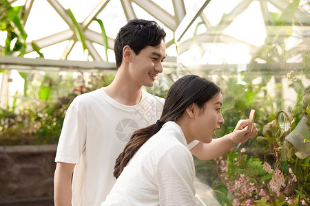 情侣在植物园拿着放大镜观察植物背景图片