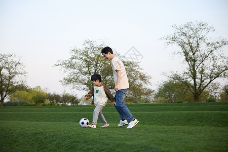 父亲和儿子在户外草地上踢足球高清图片