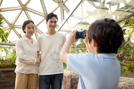 微笑合影植物园里正在给爸爸妈妈拍照的小男孩背景