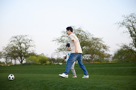 正在草坪上奔跑追球的父子俩背景