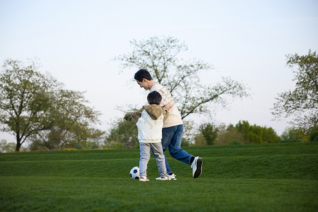 父子玩乐正在草坪上奔跑追球的父子俩背景