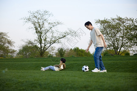 躺在草坪上的小男孩和在旁边玩球的父亲高清图片