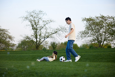 玩球的男孩躺在草坪上的小男孩和在旁边玩球的父亲背景