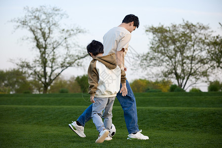 爸爸运动和爸爸在草坪上玩足球的小男孩背景