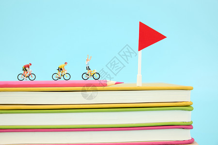 F1旗帜在一叠彩色书本上骑行冲向终点的微距小人背景