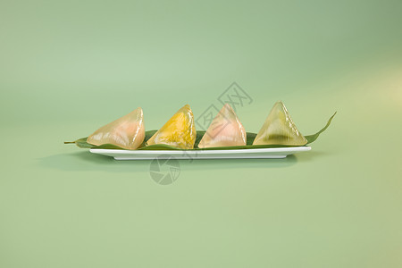 传统餐饮盘中粽叶上的四个彩色水晶粽子背景