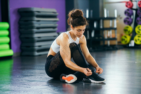 运动女子系着她的运动鞋坐健身房地板上运动女子健身房系运动鞋图片