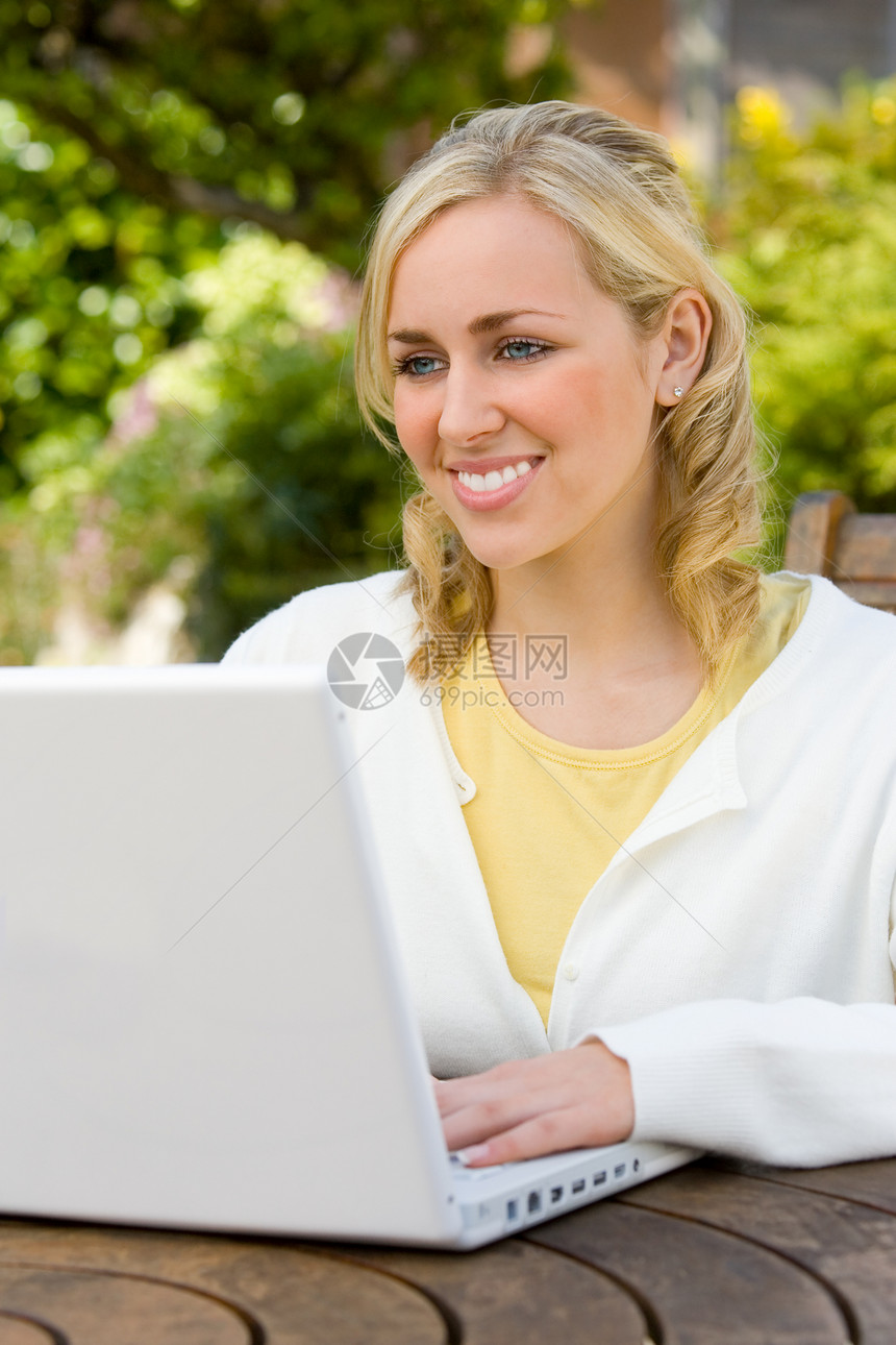 美丽快乐微笑的年轻女子十几岁的女孩,有着完美的牙齿,家里的花园里用台白色的笔记本电脑图片