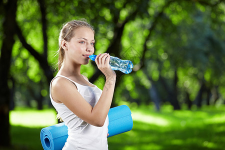 年轻迷人的女孩喝水,保持健身房的垫子图片