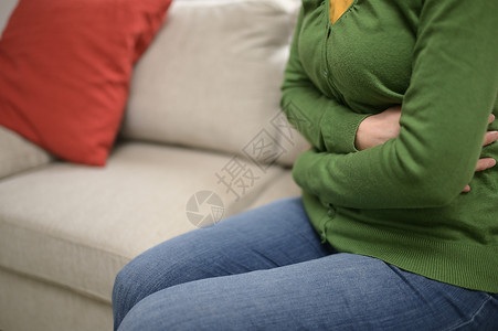 多囊卵巢综合症女人的手前胃上疼沙发上背景