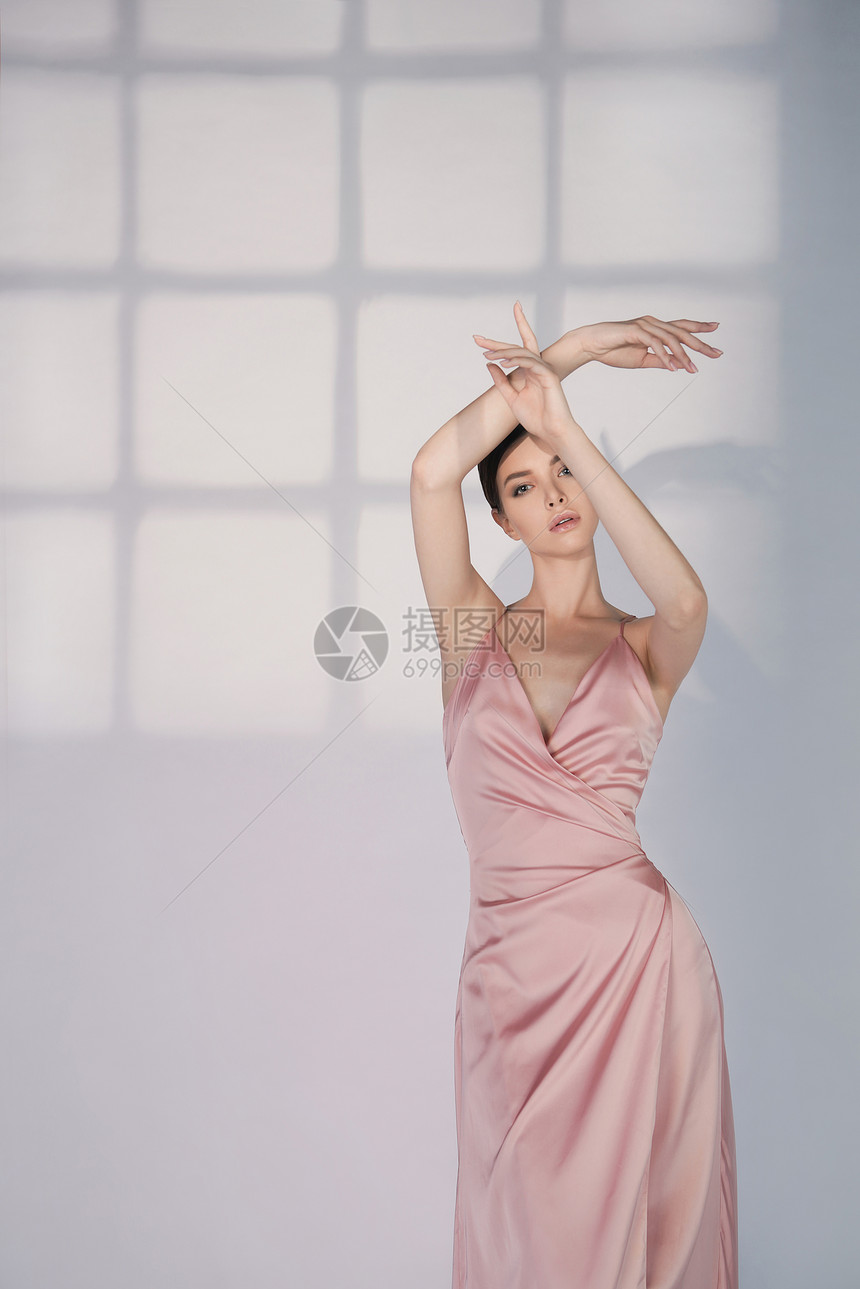 穿着优雅时尚连衣裙的女人穿着粉红色晚礼服工作室里摆着漂亮的模特姿势经典的丝绸连衣裙性感的女士保持白色背景完美的图片