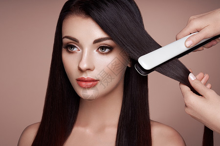 理发师用发烫把深色长发伸直长着直发的漂亮女人光滑的发型背景